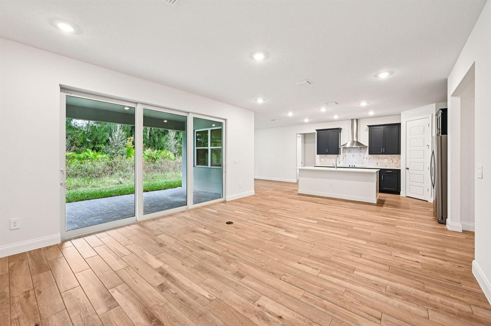 An open-concept kitchen and living area features light wood-look flooring and sliding glass patio doors — 5629 Hampton Park Circle, Vero Beach FL 32966, VERO BEACH, FL