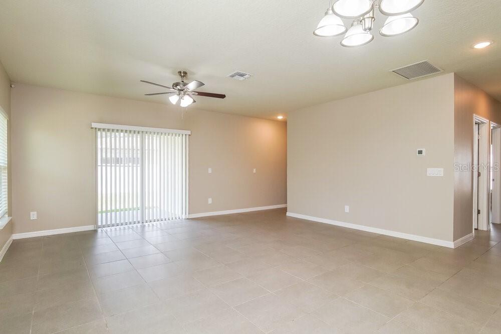 An open-concept living room features light-colored tile flooring, a ceiling fan, and sliding glass doors — 651 MERCADO COURT, KISSIMMEE, FL