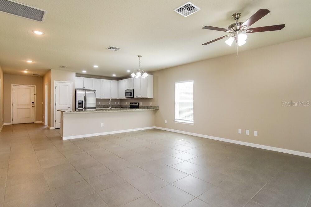 An open-concept kitchen and living area features tile flooring, white cabinetry, and a ceiling fan — 651 MERCADO COURT, KISSIMMEE, FL