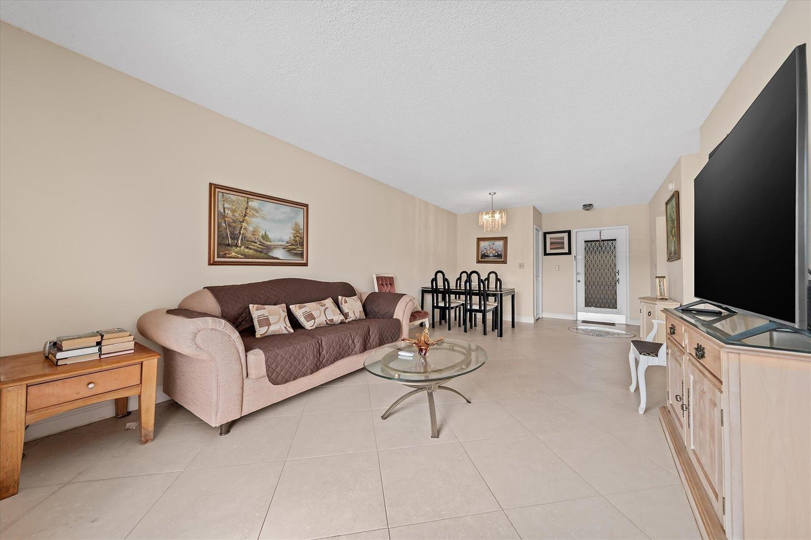 A living room with beige tile floors, a brown sofa, and a glass coffee table — 3201 NE 14th Street Causeway # 209, Pompano Beach FL 33062, POMPANO BEACH, FL