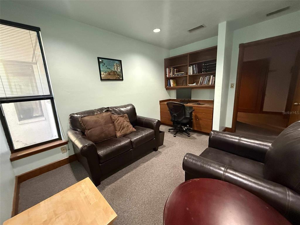 A home office features a leather sofa, a desk with built-in shelving, and carpeted flooring — 2833 NW 41ST STREET UNIT 140 Room C, GAINESVILLE, FL