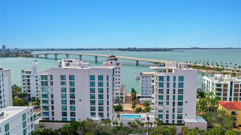 An aerial view shows several modern white apartment buildings near a bridge over the water — 223 GOLDEN GATE POINT UNIT 302, SARASOTA, FL