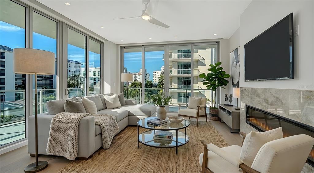 A modern living room features a sectional sofa, glass coffee table, fireplace, and floor-to-ceiling windows — 223 GOLDEN GATE POINT UNIT 302, SARASOTA, FL
