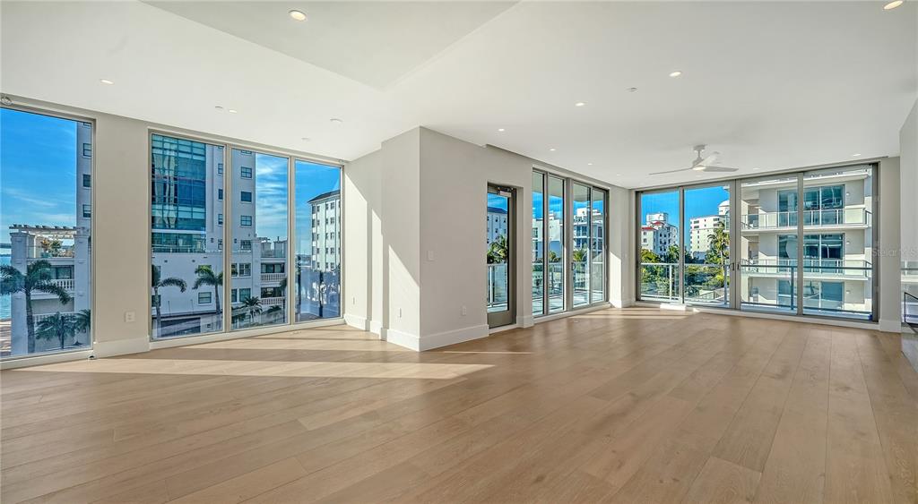 An empty living room features light wood floors, recessed lighting, and floor-to-ceiling windows — 223 GOLDEN GATE POINT UNIT 302, SARASOTA, FL