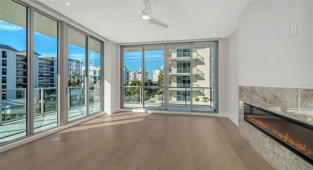 A modern living room features light wood floors, a linear fireplace, and floor-to-ceiling glass doors — 223 GOLDEN GATE POINT UNIT 302, SARASOTA, FL