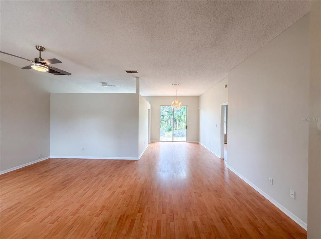 An open-concept living area features light-colored walls, wood flooring, a ceiling fan, and sliding doors — 5263 CLARION OAKS DRIVE, ORLANDO, FL