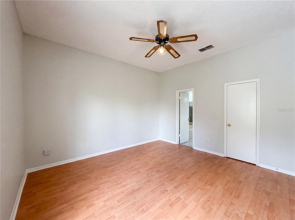 An empty bedroom features light gray walls, wood-look flooring, a ceiling fan, and two doors — 5263 CLARION OAKS DRIVE, ORLANDO, FL