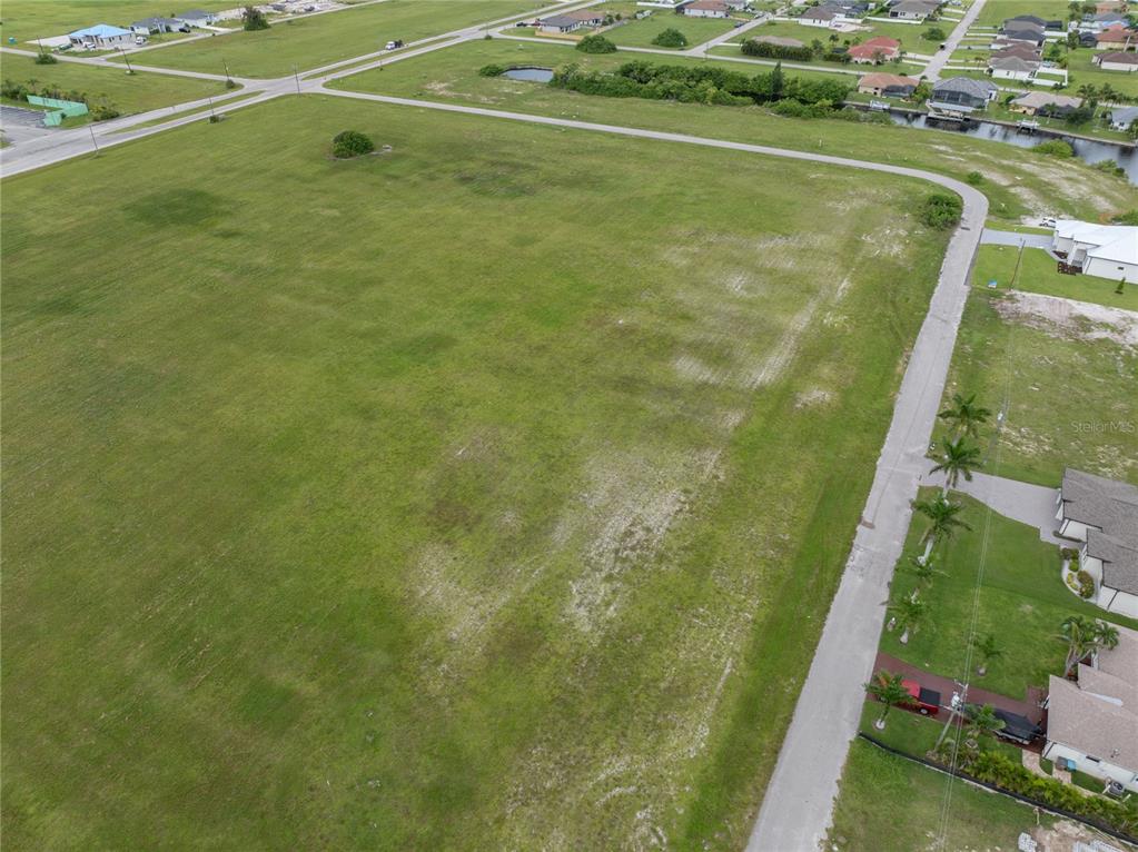 An aerial view shows a large, vacant grassy lot bordered by paved roads and residential houses — 3216 NW 9TH STREET, CAPE CORAL, FL