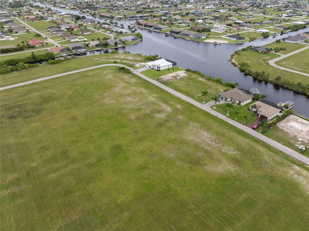 An aerial view shows a large vacant grassy lot next to a canal and houses — 3216 NW 9TH STREET, CAPE CORAL, FL