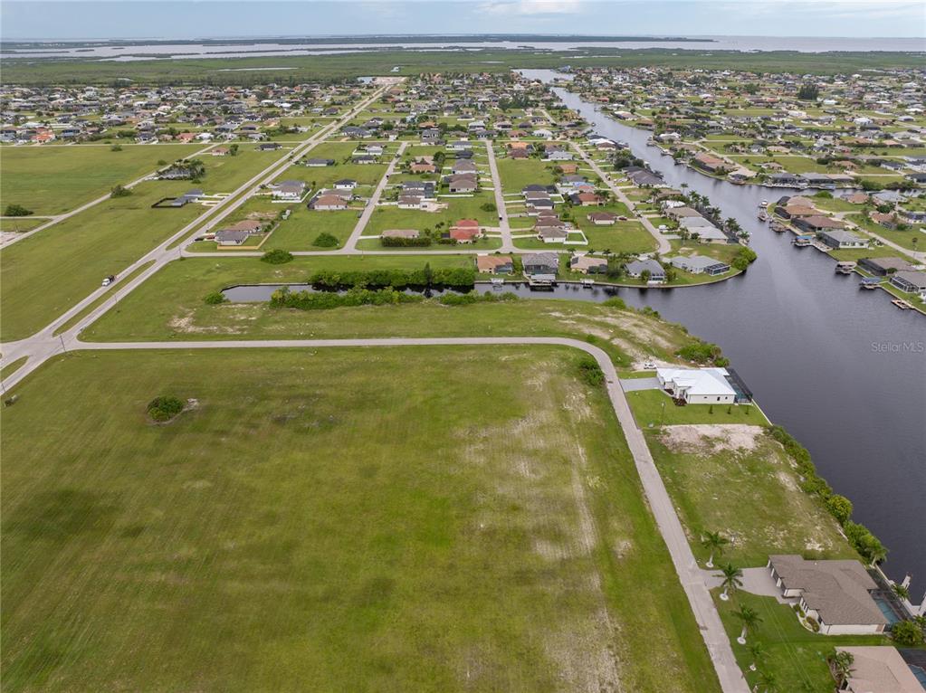 An aerial view shows a large vacant grassy lot adjacent to a canal and neighborhood — 3216 NW 9TH STREET, CAPE CORAL, FL