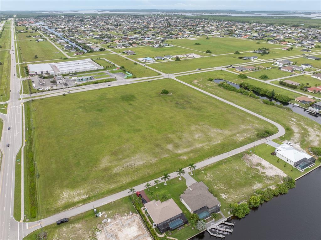An aerial view shows a large, undeveloped grassy lot bordered by roads and residential homes — 3216 NW 9TH STREET, CAPE CORAL, FL