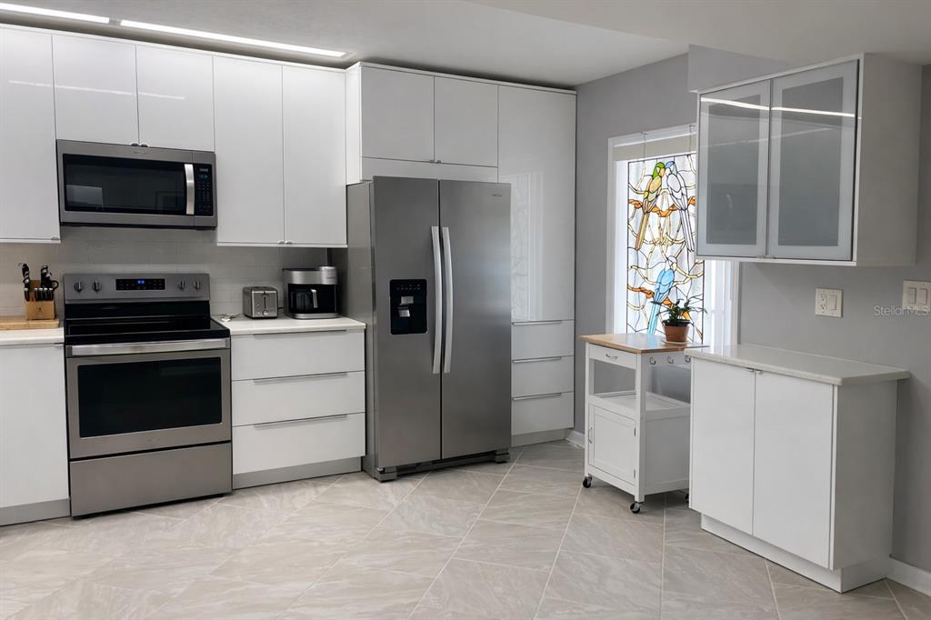 A modern kitchen features white cabinets, stainless steel appliances, and a stained-glass window — 8651 10TH STREET N UNIT 228, ST PETERSBURG, FL