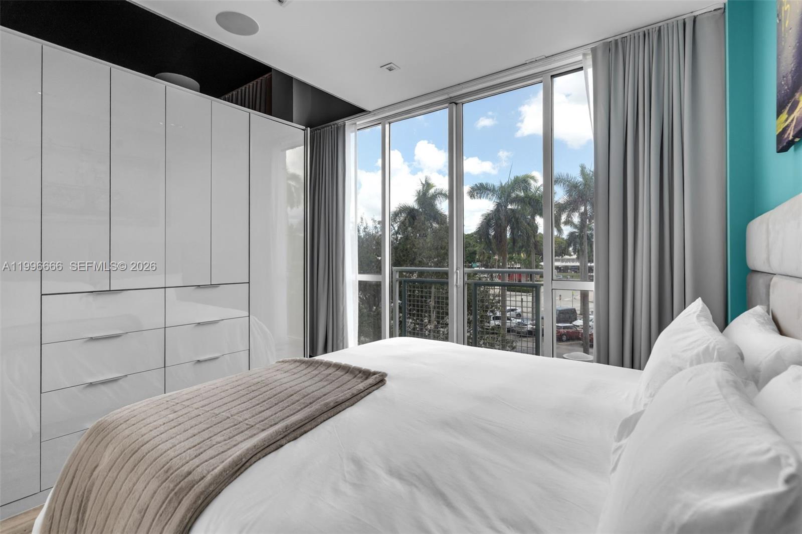 A modern bedroom features white built-in cabinetry, a bed, and floor-to-ceiling windows overlooking palm trees — 244 Biscayne Blvd # 239, Miami FL 33132, MIAMI, FL