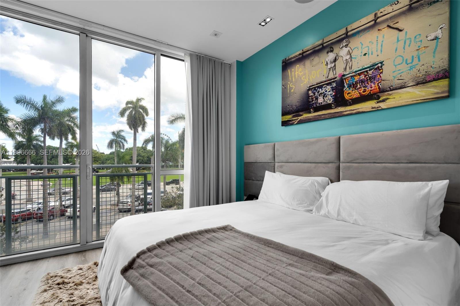 A bedroom features a bed with a grey headboard, teal wall art, and floor-to-ceiling windows — 244 Biscayne Blvd # 239, Miami FL 33132, MIAMI, FL