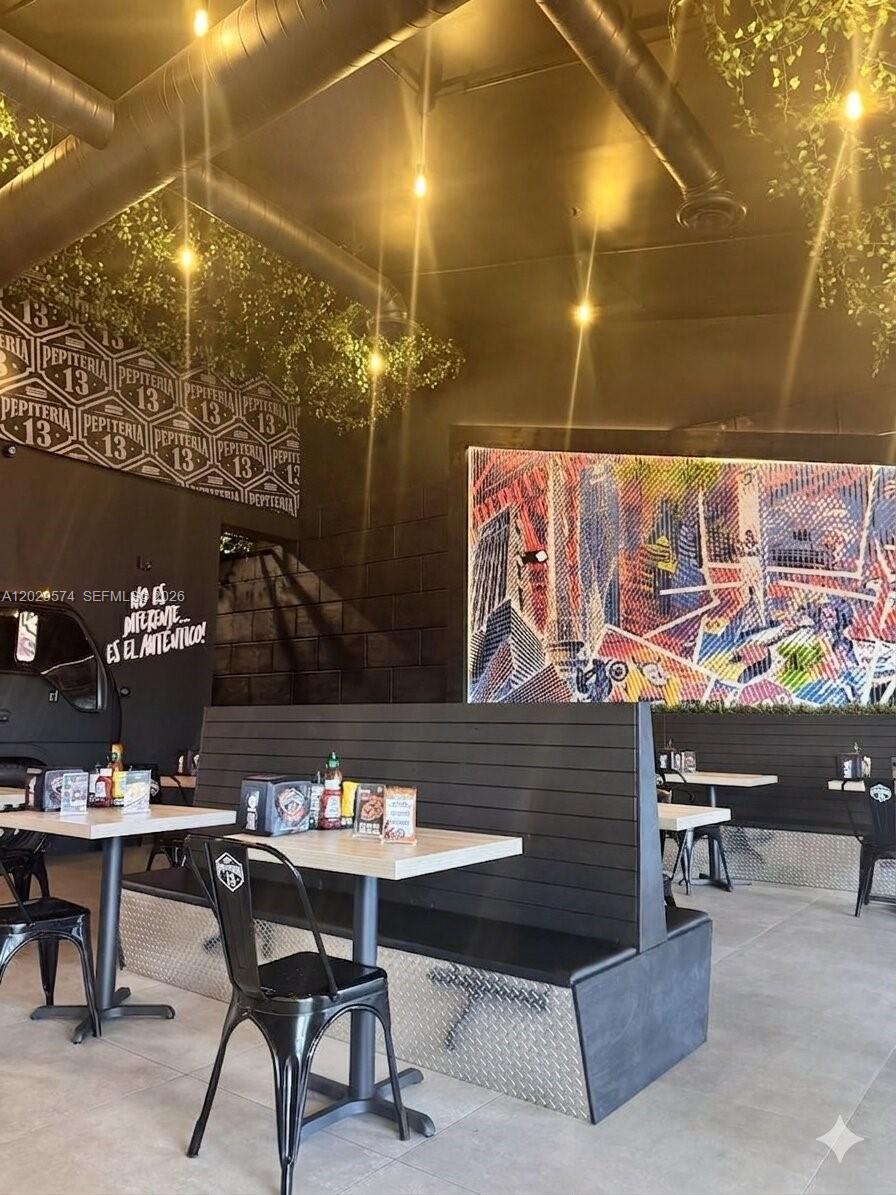 A restaurant interior features black booth seating, metal chairs, and a large colorful wall mural — 8205 NW 12th St, Doral FL 33126, DORAL, FL