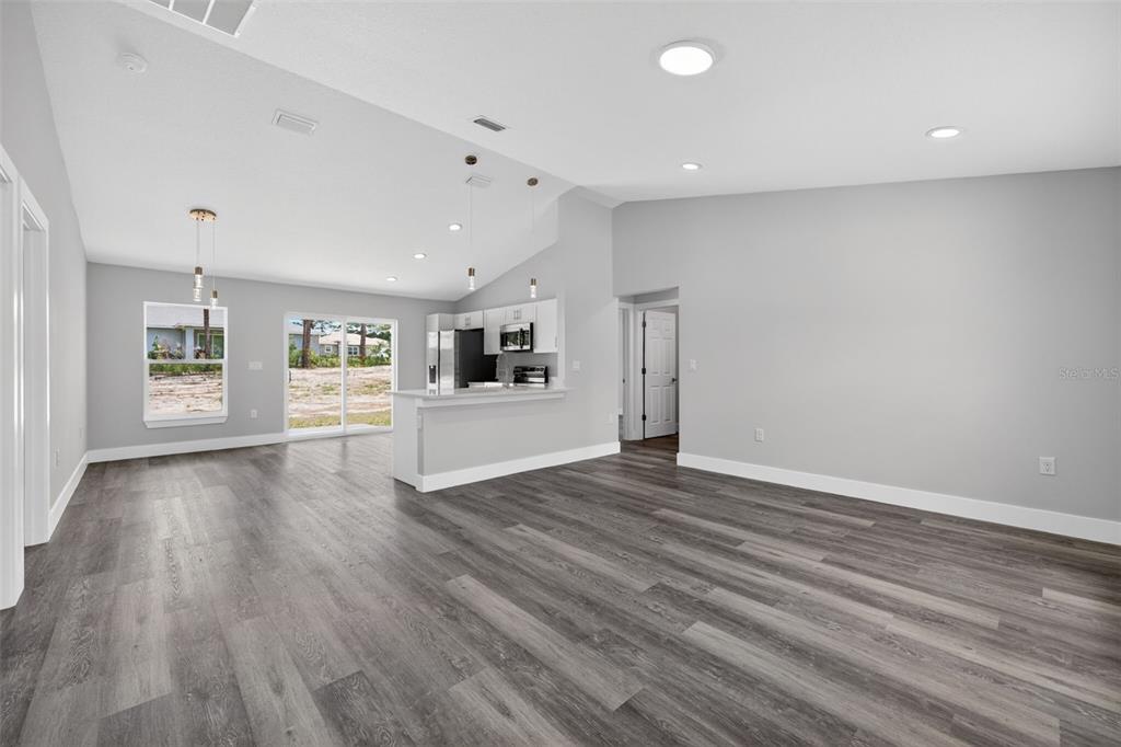 An open-concept living area features gray wood-look flooring, a kitchen island, and sliding glass doors — 1675 SW 159TH COURT, OCALA, FL