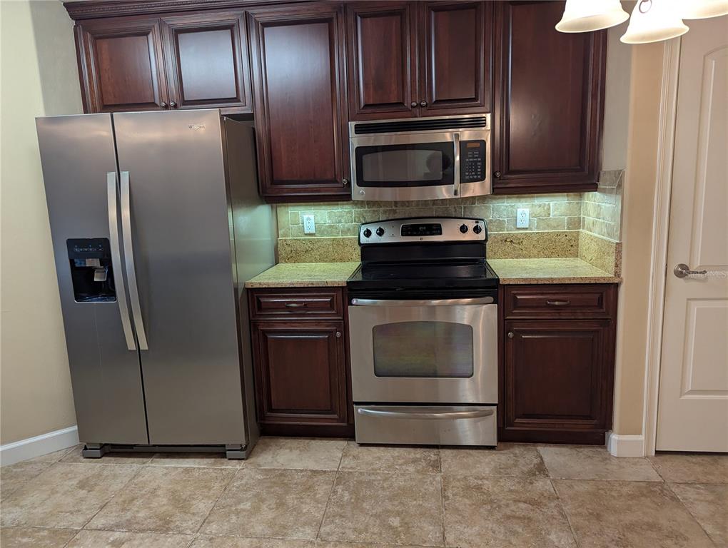 A kitchen features dark wood cabinets, stainless steel appliances, and a tan tile floor — 424 LUNA BELLA LANE UNIT 424, NEW SMYRNA BEACH, FL