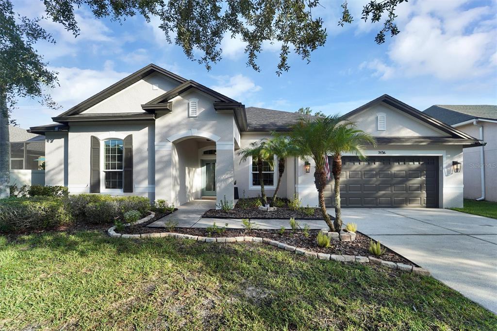 A single-story house with a beige stucco exterior, dark shutters, and a two-car garage — 7136 DERWENT GLEN CIRCLE, LAND O LAKES, FL