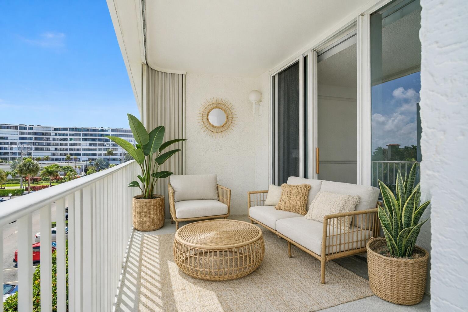 A balcony features wicker furniture, a neutral rug, two potted plants, and a sunburst mirror — 3580 S Ocean Boulevard # 4c, South Palm Beach FL 33480, SOUTH PALM BEACH, FL