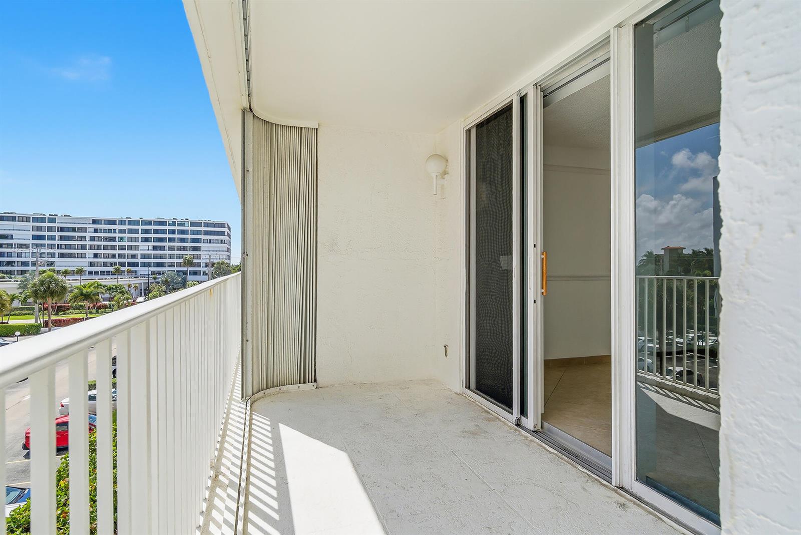 A balcony with a white metal railing overlooks a parking lot and a large building — 3580 S Ocean Boulevard # 4c, South Palm Beach FL 33480, SOUTH PALM BEACH, FL