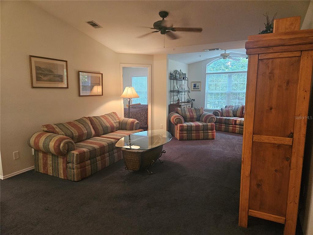 A living room features a striped sofa, matching armchairs, a glass coffee table, and carpeting — 13810 SUTTON PARK DRIVE N UNIT 738, JACKSONVILLE, FL