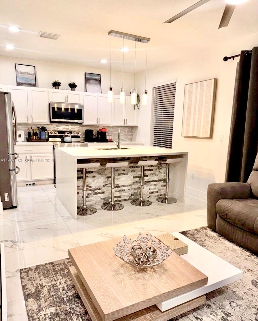 A modern kitchen features white cabinetry, a stone-tiled island with bar stools, and tile flooring — 4237 SW 164th Path # 4237, Miami FL 33185, MIAMI, FL