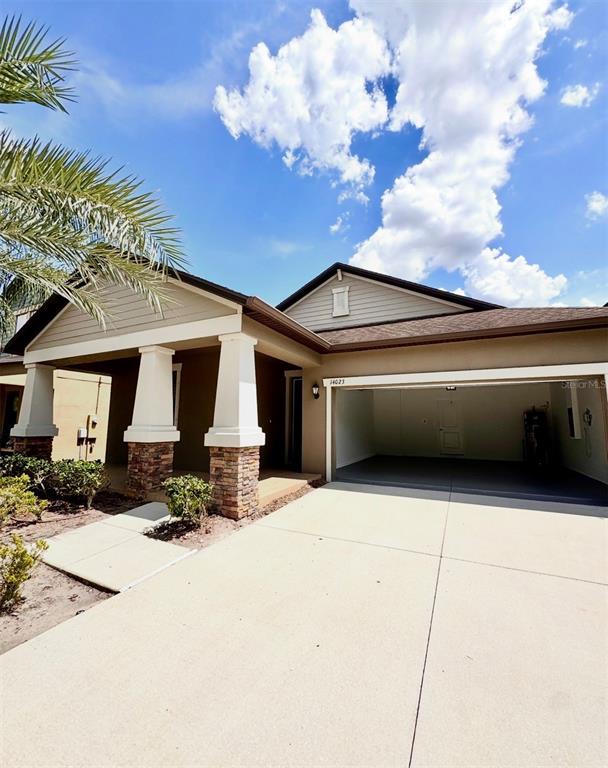 A single-story house exterior features a covered porch with stone columns and an open garage — 14023 TROPICAL KINGBIRD WAY, RIVERVIEW, FL