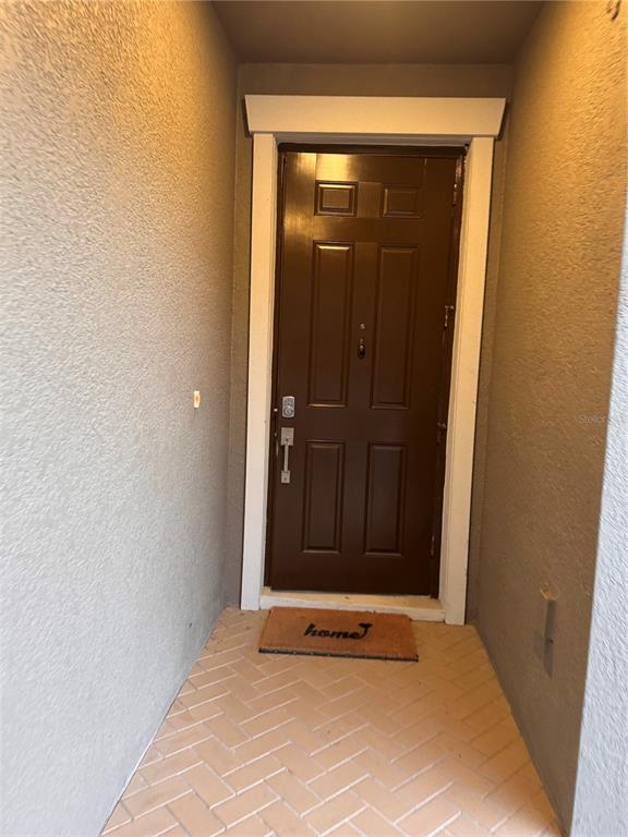 A brown front door with a welcome mat sits at the end of a covered entryway — 14023 TROPICAL KINGBIRD WAY, RIVERVIEW, FL