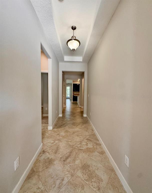 A hallway with beige walls, tile flooring, and a recessed ceiling with a pendant light — 14023 TROPICAL KINGBIRD WAY, RIVERVIEW, FL