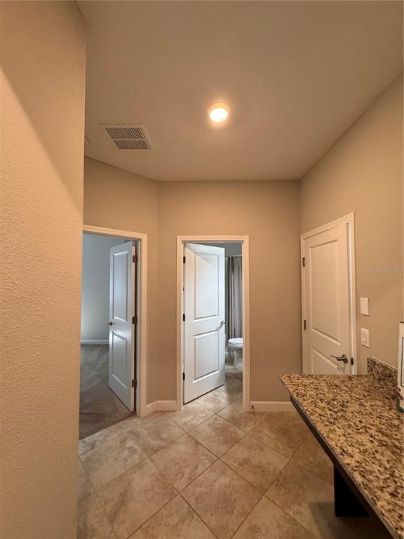 A hallway with tile flooring leads to two doorways and a granite-topped counter — 14023 TROPICAL KINGBIRD WAY, RIVERVIEW, FL