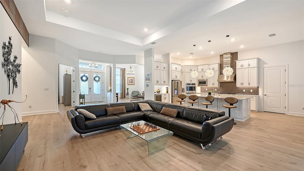 A modern open-concept living room and kitchen with white cabinetry, a large sectional, and flooring — 9483 TEQUILA SUNRISE DRIVE, SARASOTA, FL