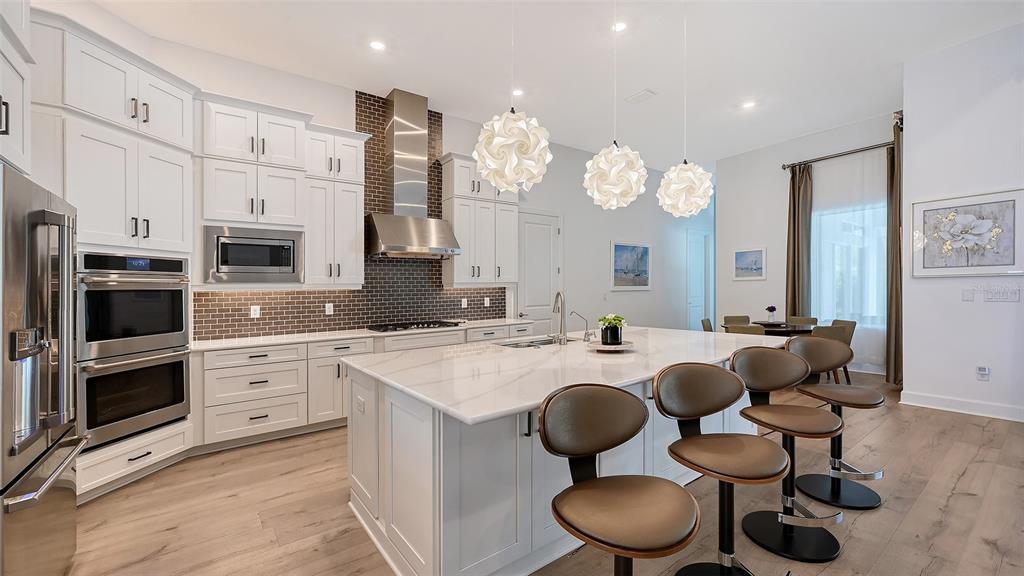 A modern kitchen features white cabinetry, a large marble-topped island, and three pendant lights — 9483 TEQUILA SUNRISE DRIVE, SARASOTA, FL