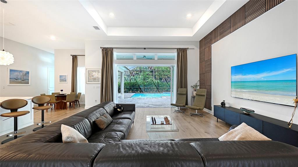 A modern living room features a large leather sectional, a wall-mounted television, and sliding glass doors — 9483 TEQUILA SUNRISE DRIVE, SARASOTA, FL