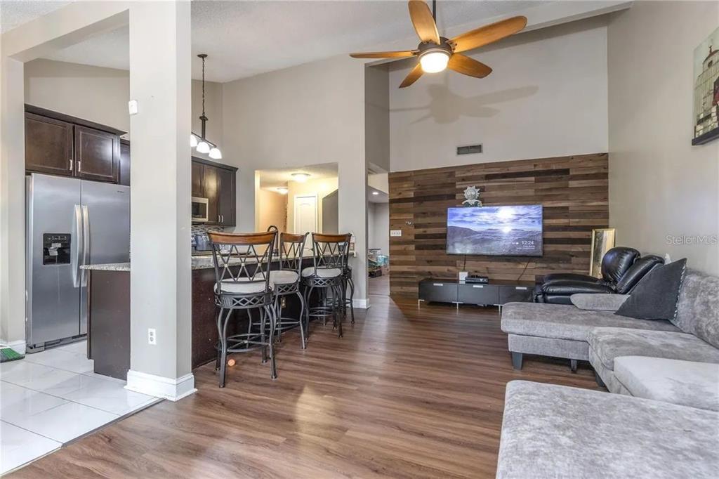 An open-concept living room and kitchen featuring wood-plank walls, a ceiling fan, and bar seating — 6334 QUAIL RIDGE DRIVE, TAMPA, FL