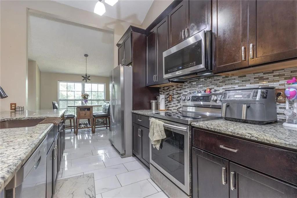 A kitchen with dark wood cabinets, stainless steel appliances, granite countertops, and white tile flooring — 6334 QUAIL RIDGE DRIVE, TAMPA, FL