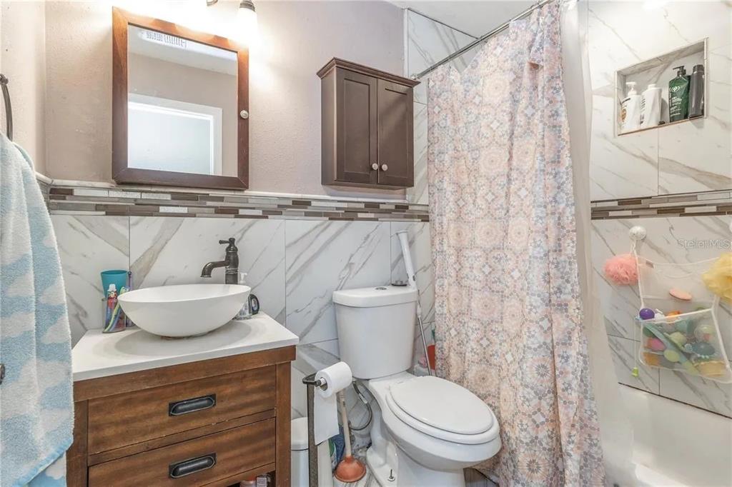 A bathroom features a vessel sink vanity, a toilet, and a shower with marble-look tiles — 6334 QUAIL RIDGE DRIVE, TAMPA, FL