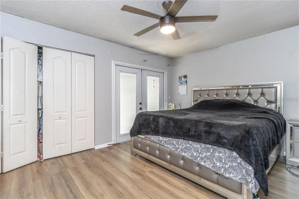 A bedroom features light wood-look flooring, a tufted headboard, a ceiling fan, and sliding doors — 6334 QUAIL RIDGE DRIVE, TAMPA, FL