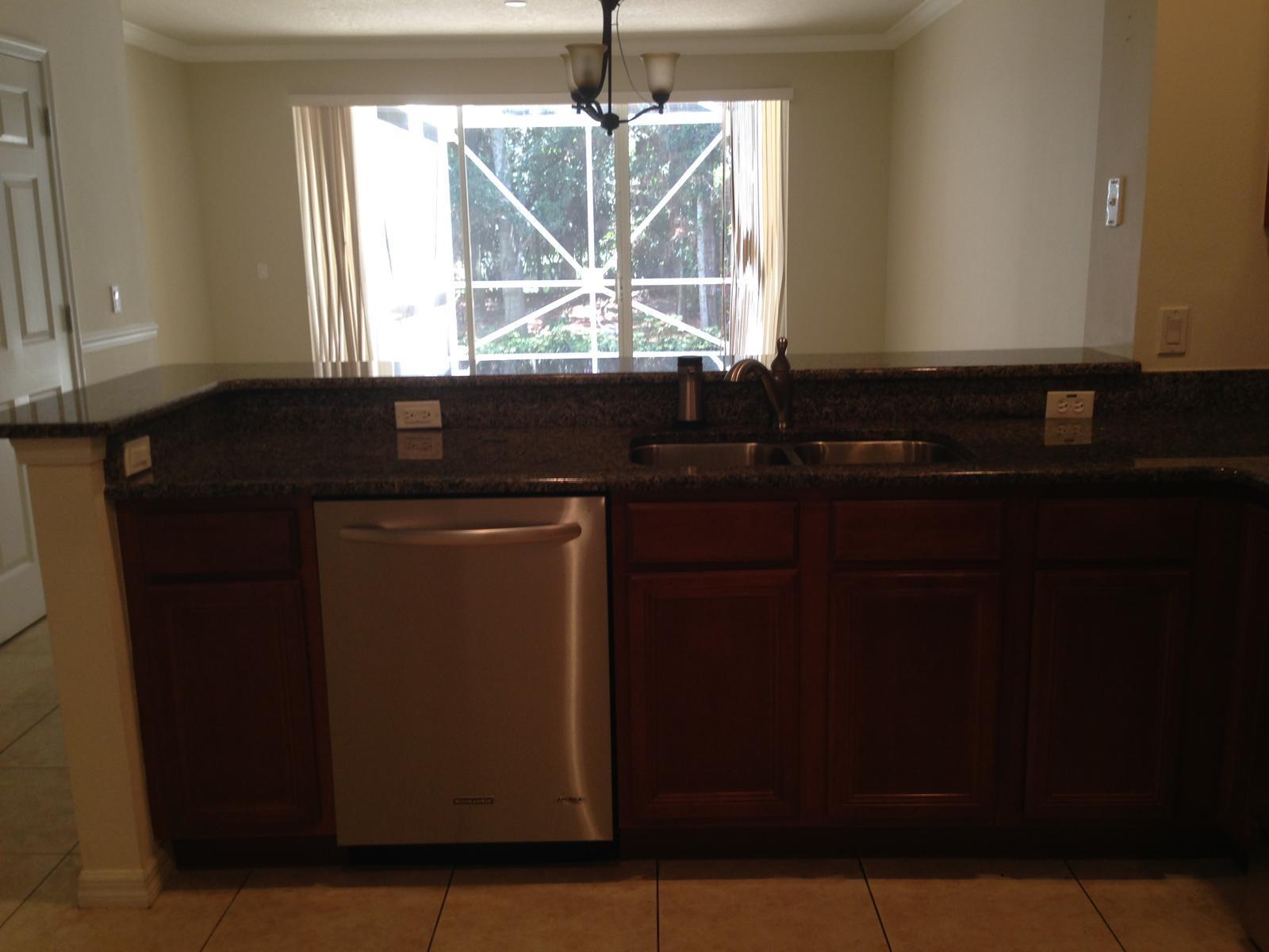 A kitchen sink and dishwasher are set into a dark granite countertop with wood cabinets — 9680 Lago Drive # 9680, Boynton Beach FL 33472, BOYNTON BEACH, FL