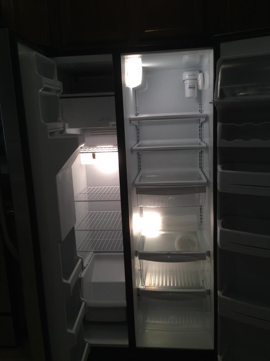 An open side-by-side refrigerator with interior lighting, wire shelves, and clear plastic drawers — 9680 Lago Drive # 9680, Boynton Beach FL 33472, BOYNTON BEACH, FL