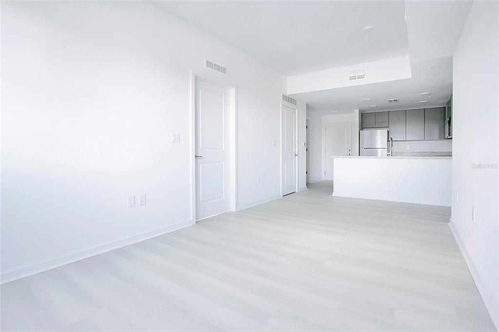 An interior view of a bright, minimalist living area with light wood floors and a kitchen — 5579 MILLENIA PARK BOULEVARD UNIT 223, ORLANDO, FL