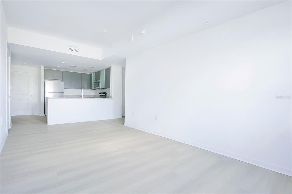 A bright, open-concept living area features light wood-look flooring and an adjacent modern kitchen — 5579 MILLENIA PARK BOULEVARD UNIT 223, ORLANDO, FL