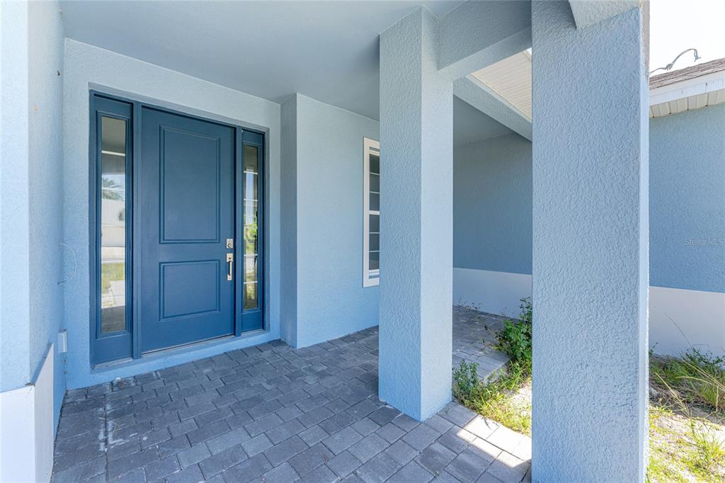 A blue front door with sidelights sits under a covered porch with stone pavers — 9024 EVELYN ROAD, ENGLEWOOD, FL
