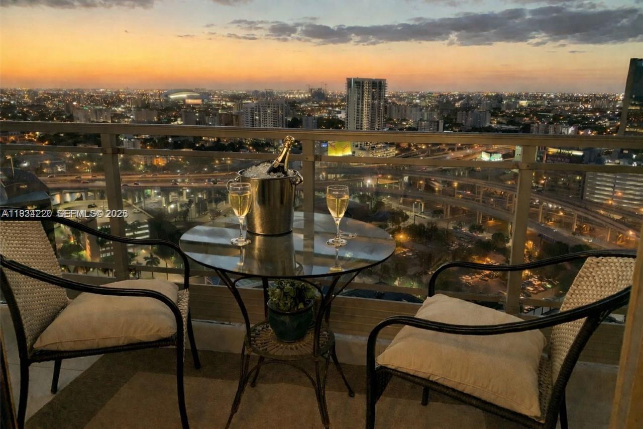 A balcony with a small table, two chairs, and champagne overlooking a city skyline at sunset — 90 SW 3rd St # 2109, Miami FL 33130, MIAMI, FL