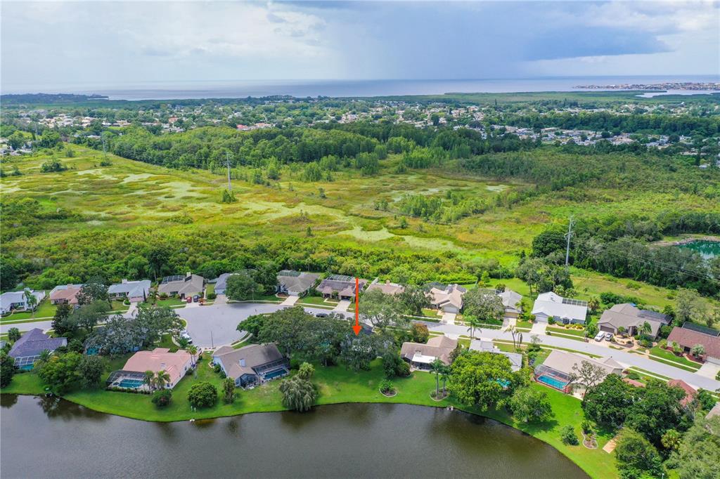 An aerial view shows a suburban neighborhood with houses bordering a lake and green space — 2906 WINDRIDGE DRIVE, HOLIDAY, FL