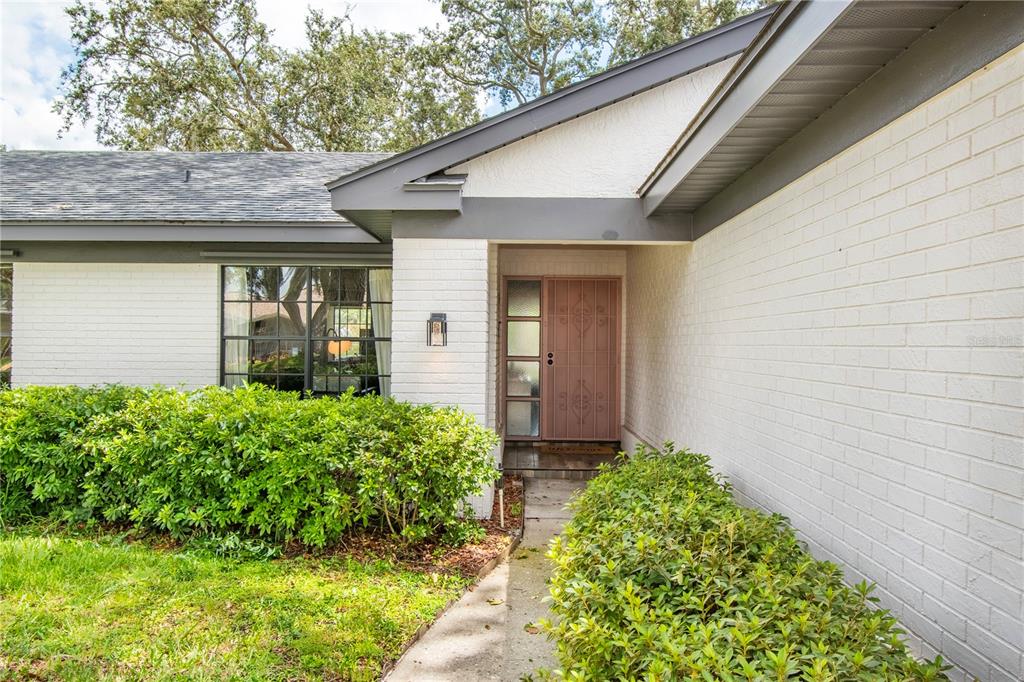 The exterior of a house features white brick walls, a dark trim, and a front door — 2906 WINDRIDGE DRIVE, HOLIDAY, FL