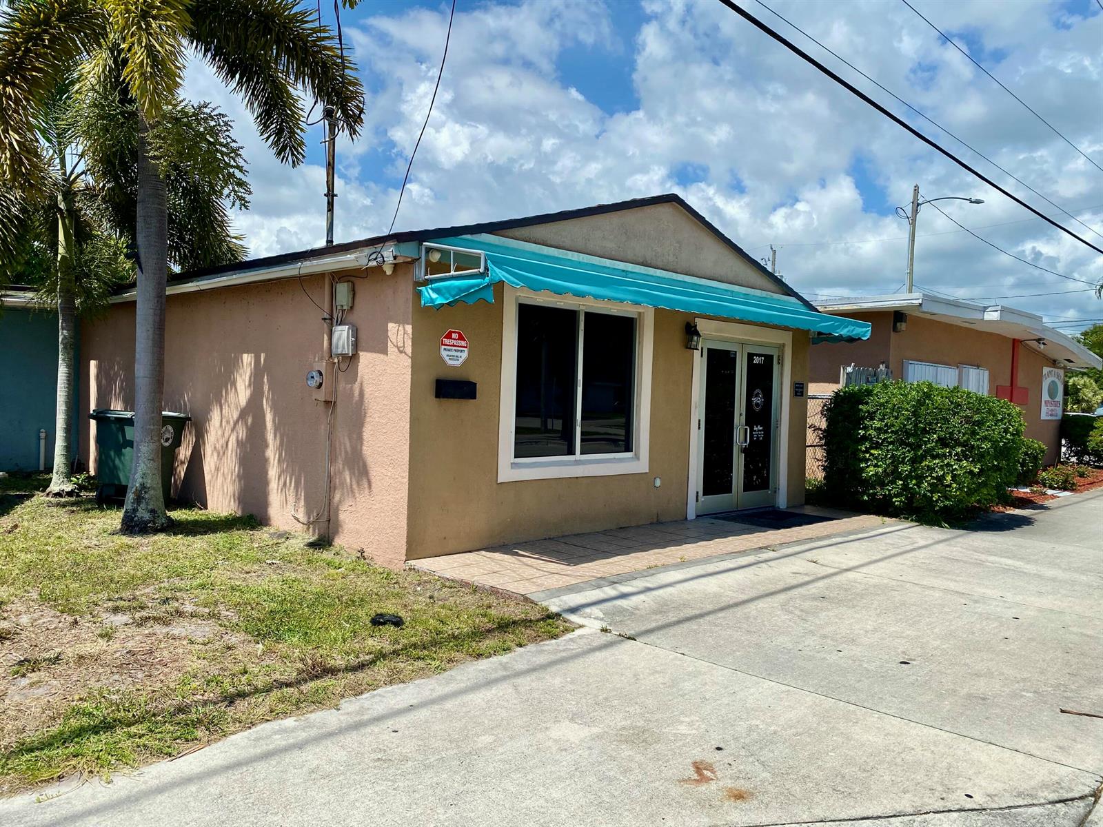 A tan, single-story commercial building features a blue awning, a large window, and a glass door — 2017 Ave D, Fort Pierce FL 34950, FORT PIERCE, FL