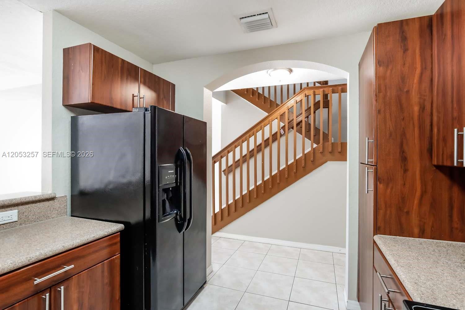 A kitchen with dark wood cabinets and a black refrigerator opens to a wooden staircase — CUTLER BAY, FL