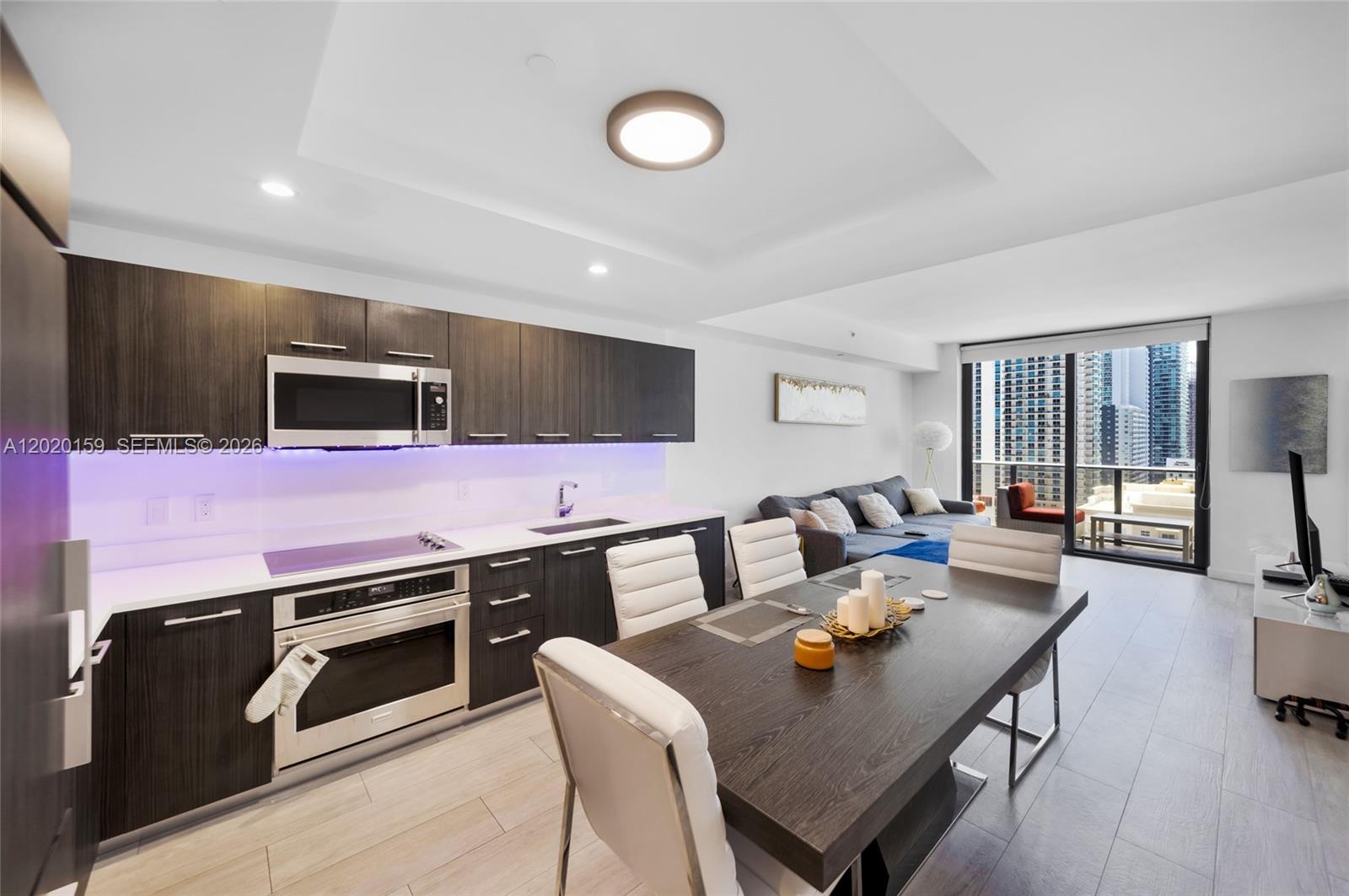 A modern kitchen and dining area with dark cabinetry, white countertops, and city balcony views — 55 SW 9th St # 1804, Miami FL 33130, MIAMI, FL