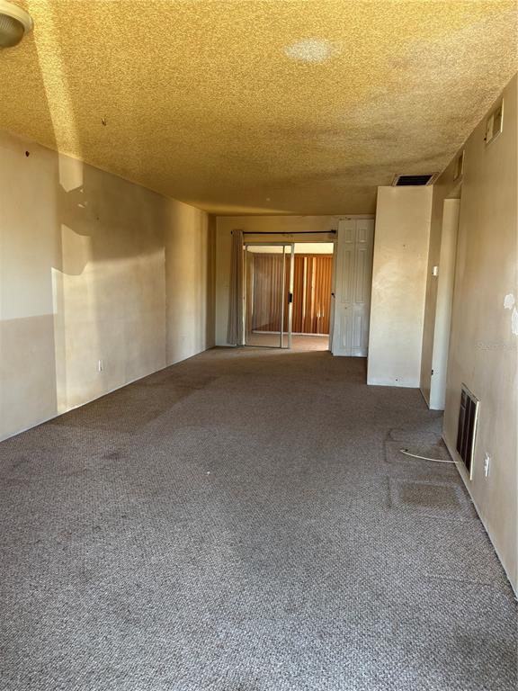 An empty living room features beige carpeting, textured ceilings, and a sliding glass door — 24862 US HIGHWAY 19 N UNIT 2803, CLEARWATER, FL