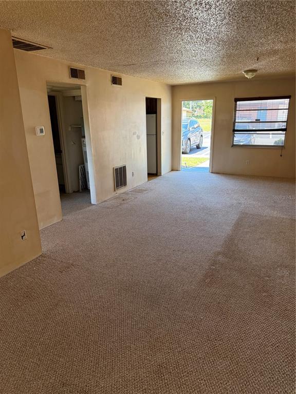 An interior view of a carpeted living room with beige walls, a doorway, and a window — 24862 US HIGHWAY 19 N UNIT 2803, CLEARWATER, FL